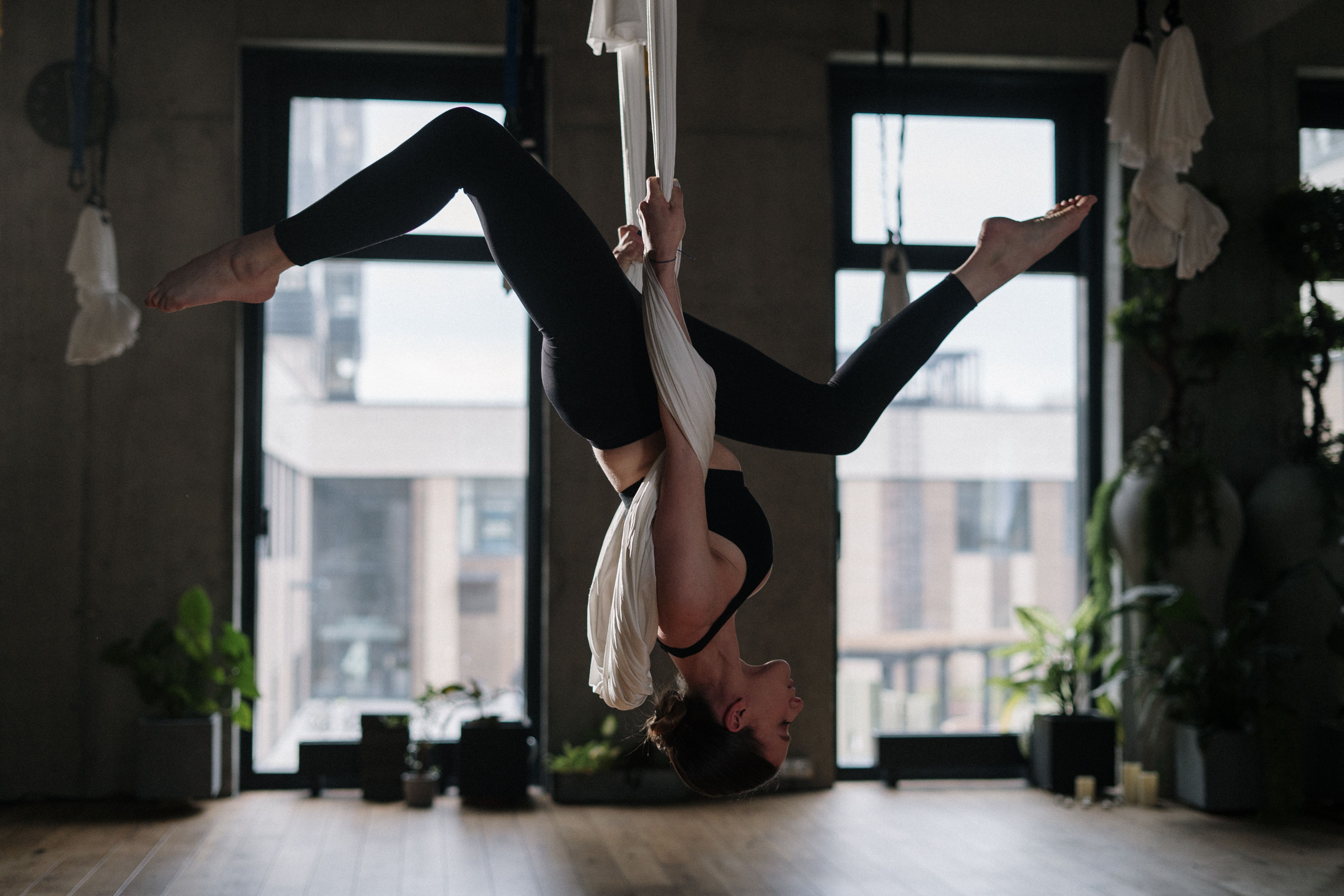 Woman practising aerial yoga in a silk hammock in a bright studio