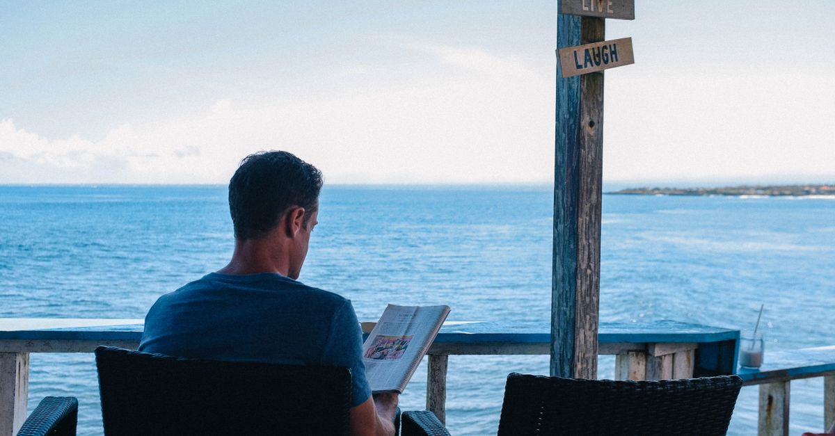 A man relaxes with a book overlooking the ocean in Bali, enjoying leisure time.
