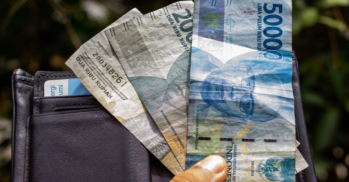 Hand holding Indonesian rupiah banknotes and a wallet, the everyday cash you carry in Bali
