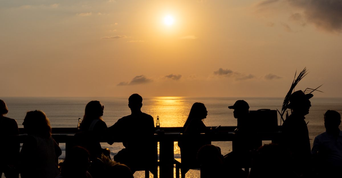Silhouettes of people drinking at a Bali beachside bar as the sun sets over the sea