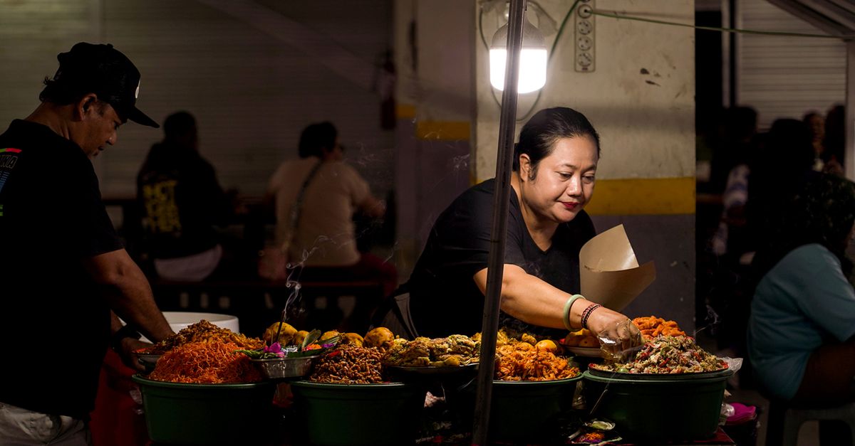 Woman serving traditional street food at a night market in Bali, Indonesia.