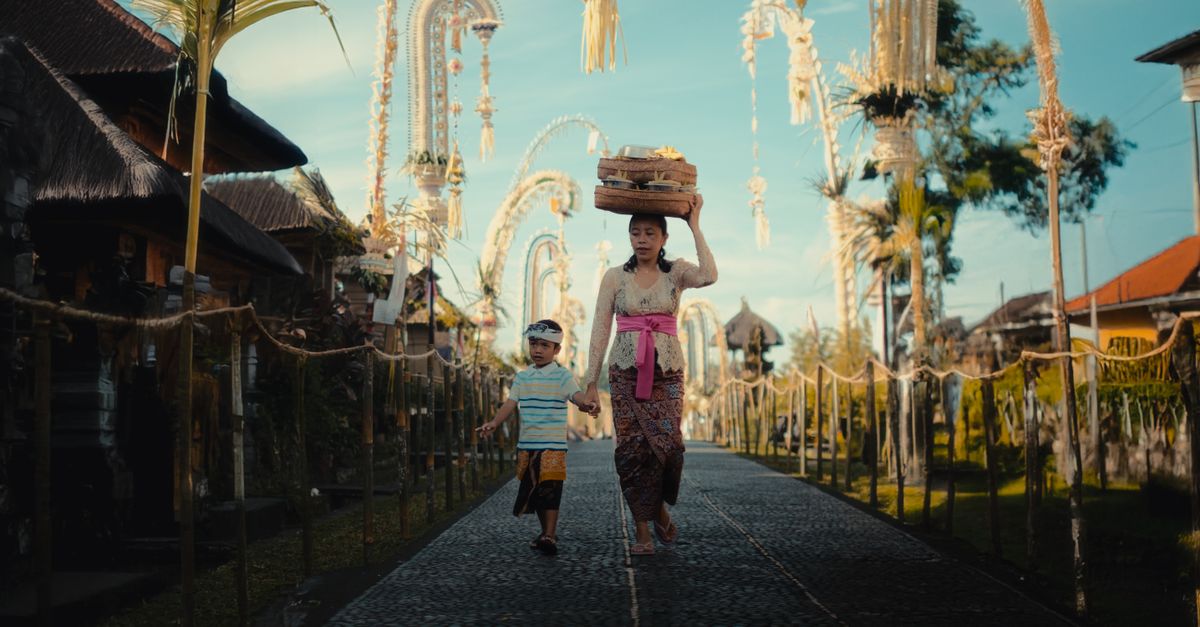 A Balinese mother and child walking in a decorated village street, showcasing cultural beauty.