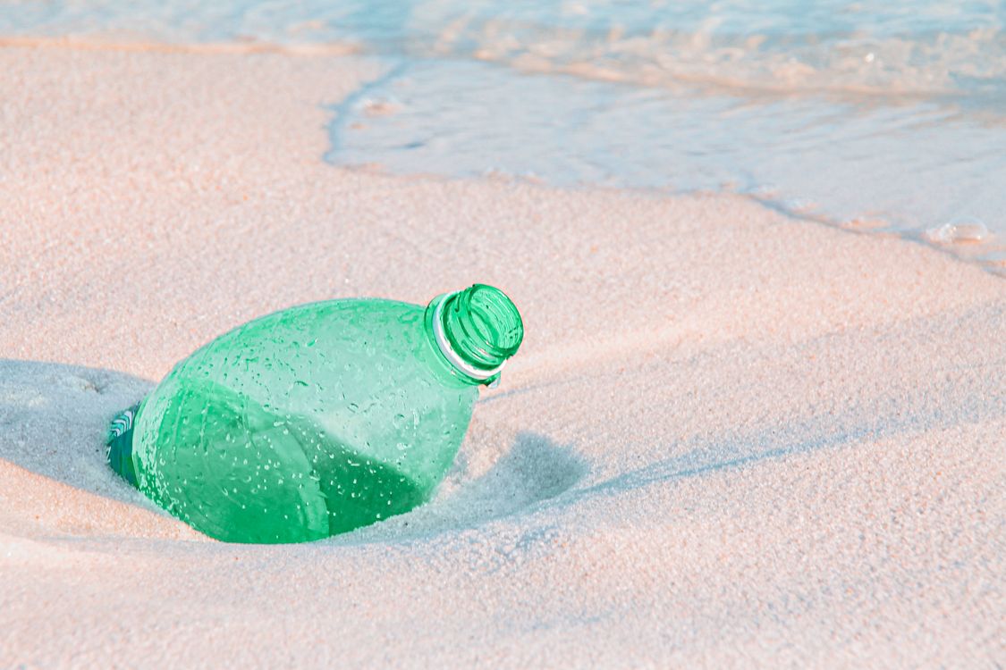A discarded plastic bottle half-buried in beach sand