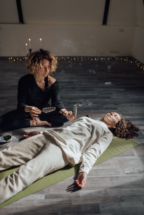 A therapist holding healing incense near a woman during a traditional wellness session