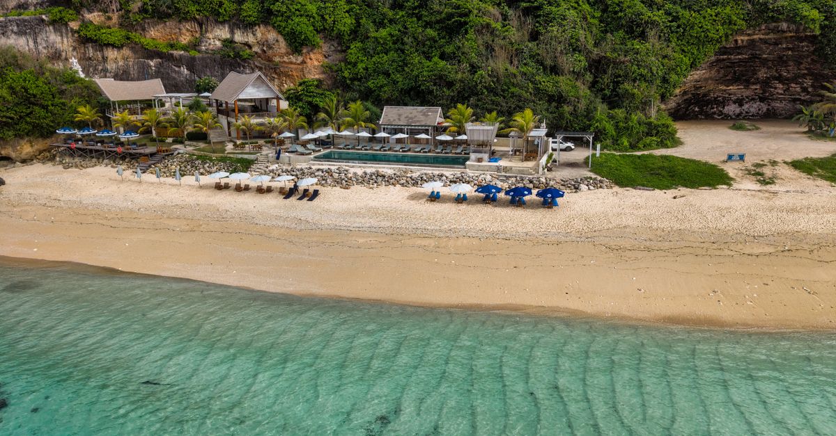 Aerial view of a beachfront resort in Bali with turquoise water and palm-lined shore