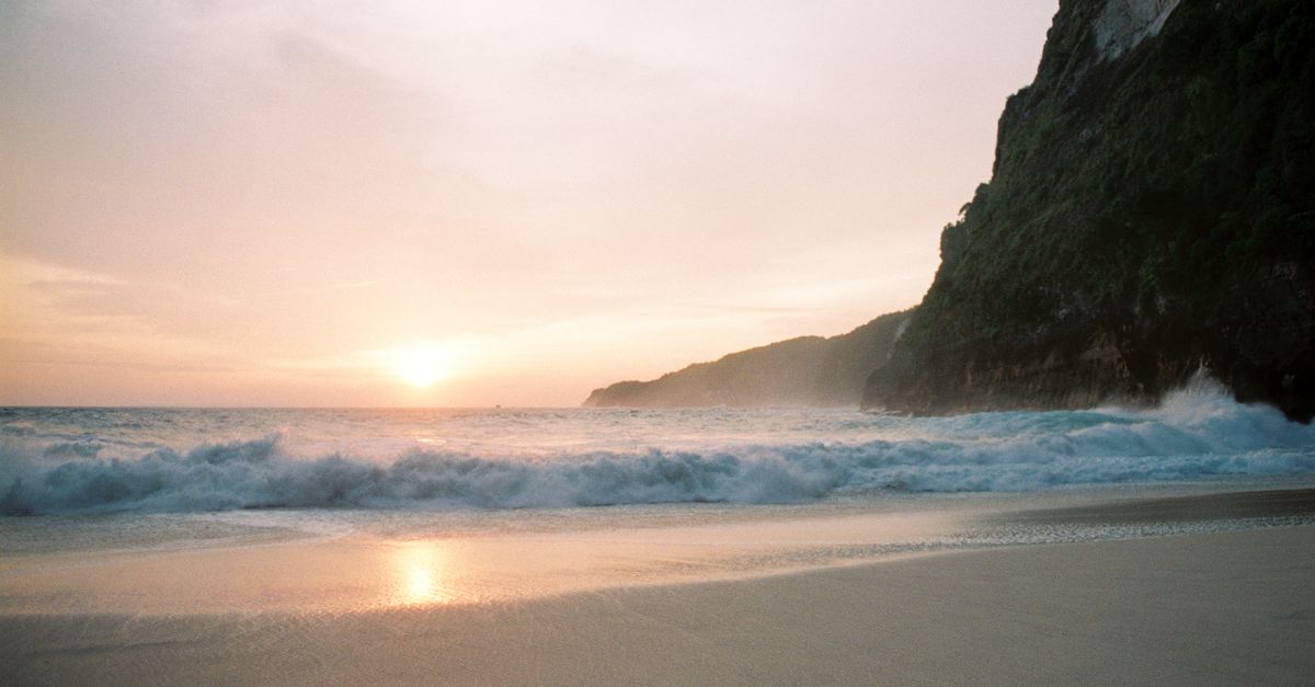 A peaceful Bali beach at sunset with waves breaking below a rocky cliff
