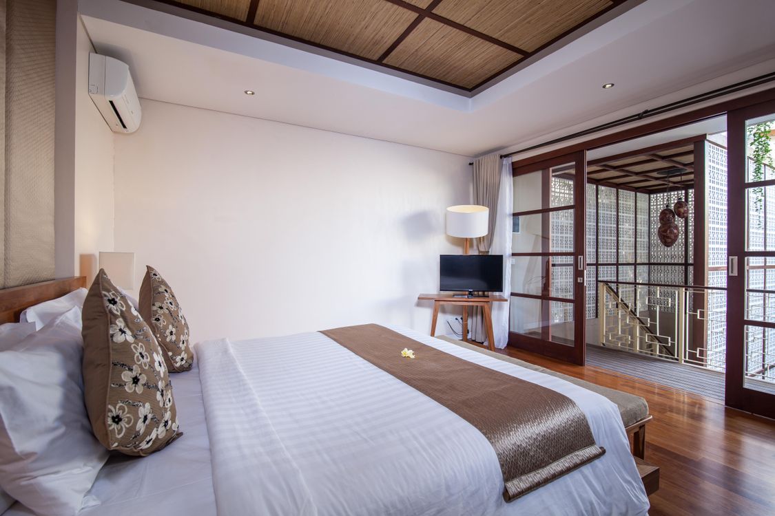 A villa bedroom in Bali with wooden flooring and a bed made up in white linen