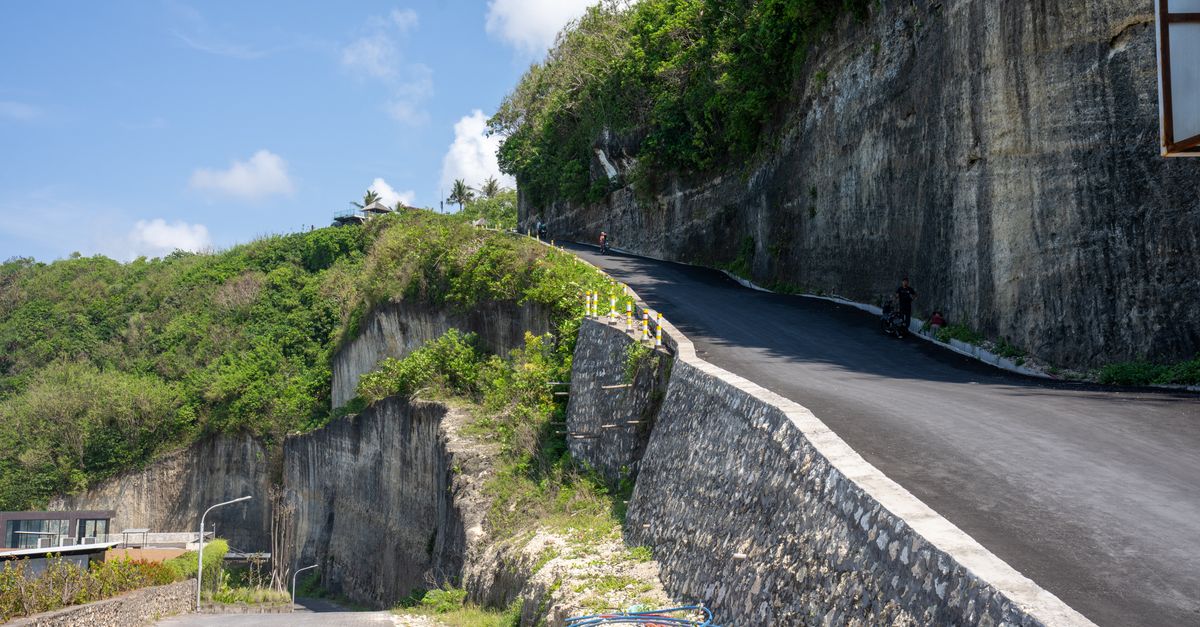 A winding cliff road through lush green hills in Bali, Indonesia under a blue sky