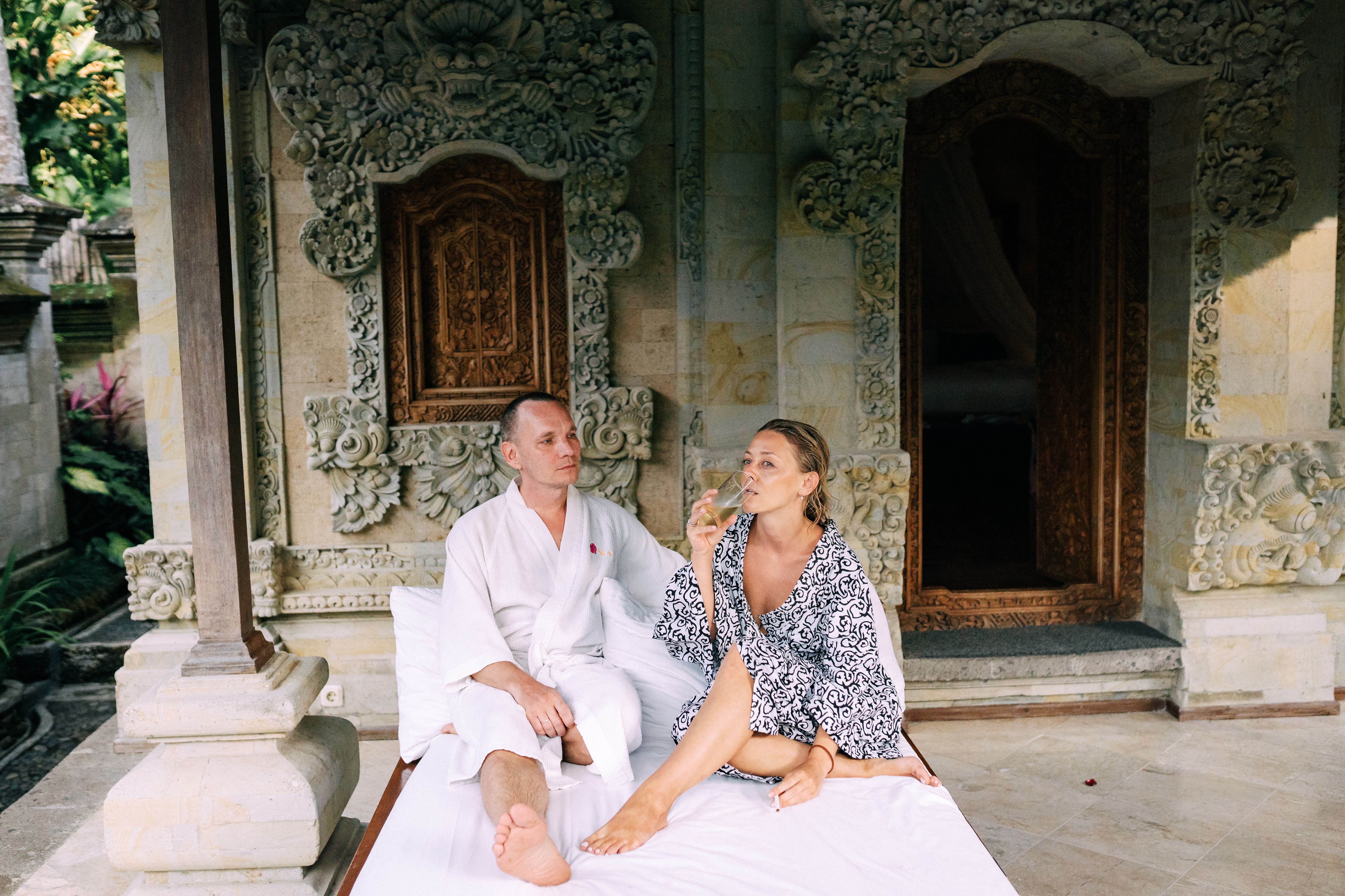 A couple relaxing outside a traditional Balinese villa with ornate carvings