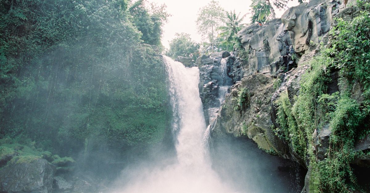 A waterfall cascading down rocky cliffs surrounded by lush green jungle in North Bali, Indonesia