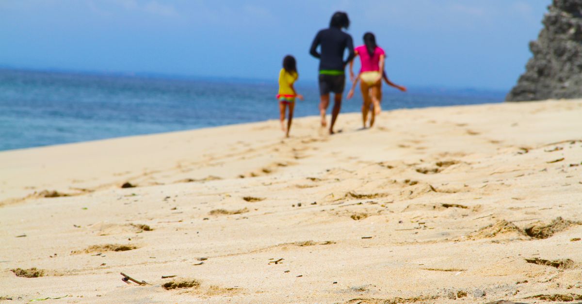 A family strolls along a sandy beach under a bright summer sky, enjoying leisure and nature.
