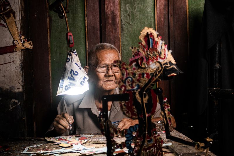 An Indonesian craftsman carefully creating a traditional wayang kulit puppet from leather