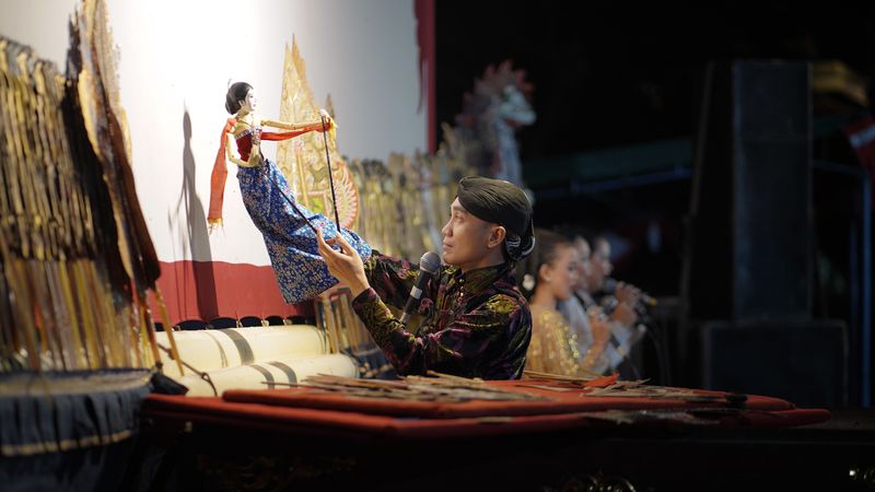 A puppeteer performing a traditional wayang kulit show, manipulating leather puppets behind a lit screen