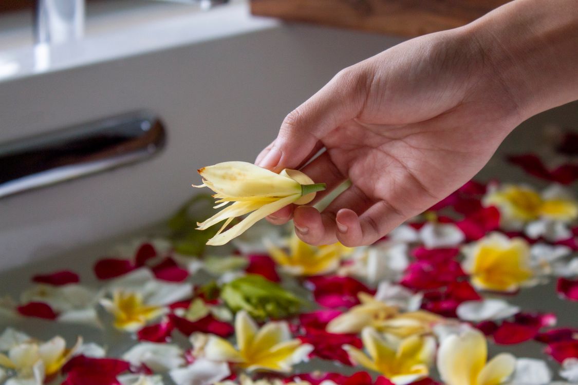 Hand holding a flower over a petal-filled flower bath at a spa in Bali