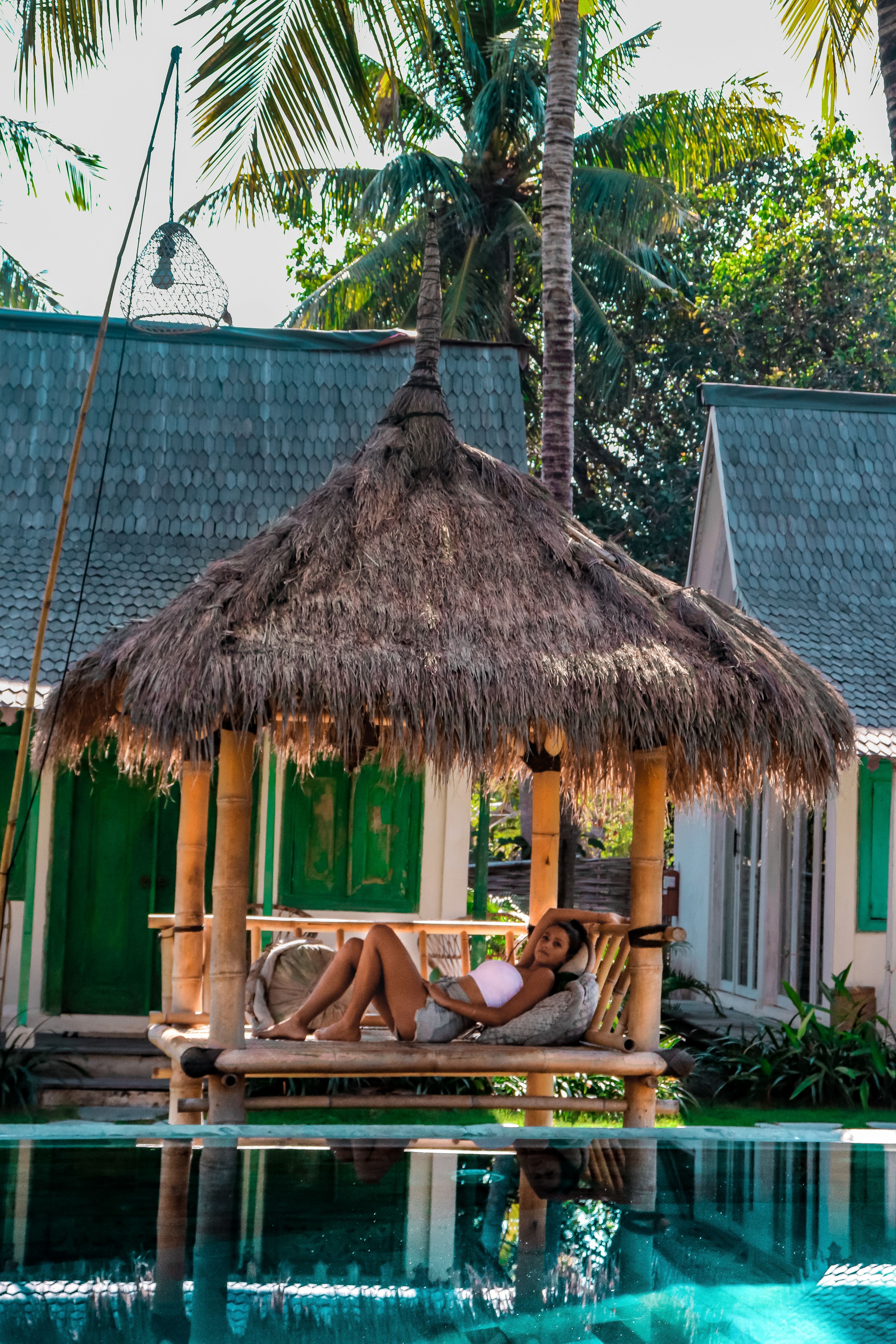 Woman relaxing in a thatched poolside hut surrounded by palm trees